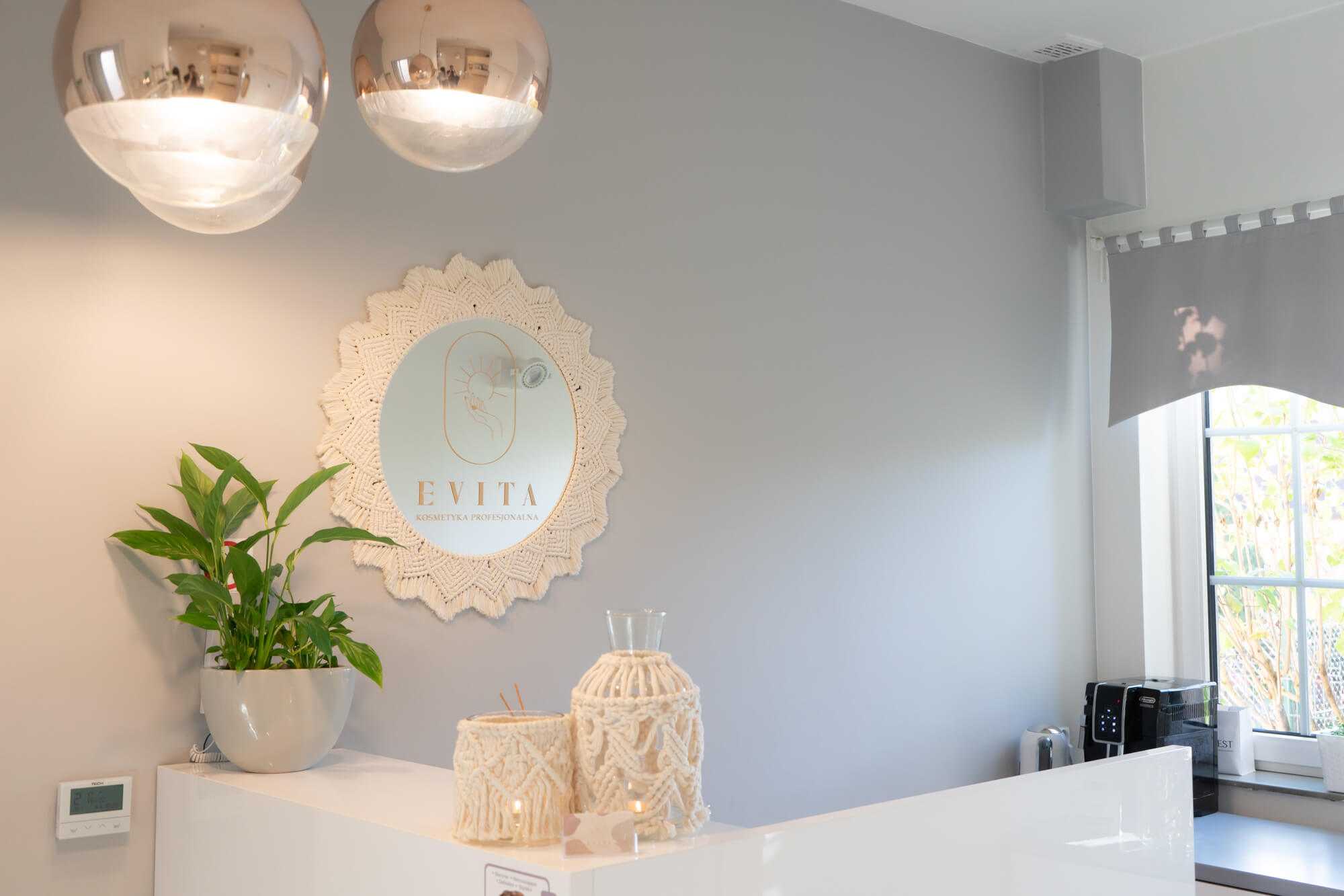Recepcja w Salonie Kosmetyki Profesjonalnej „Evita” z makramowym lustrem ze złotym logo, lampionami i złotymi lampami